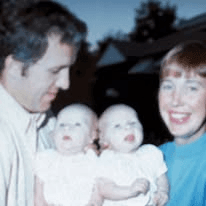 A man and a woman each holding one of two infant twins dressed in white.