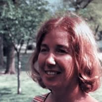 Color snapshot of a smiling woman with red hair outdoors among trees, from the Roberts family archive.