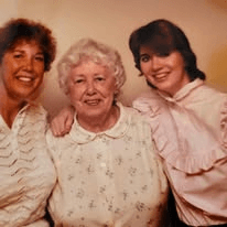 Three women side by side, the eldest in the middle in a floral top.